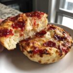A close-up of a pepperoni english muffin pizza, split in half showing melted cheese and fluffy interior.