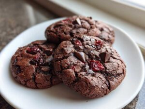 Close-up of three decadent cherry chocolate mocha cookies on a white plate, featuring dark chocolate and dried cherries.