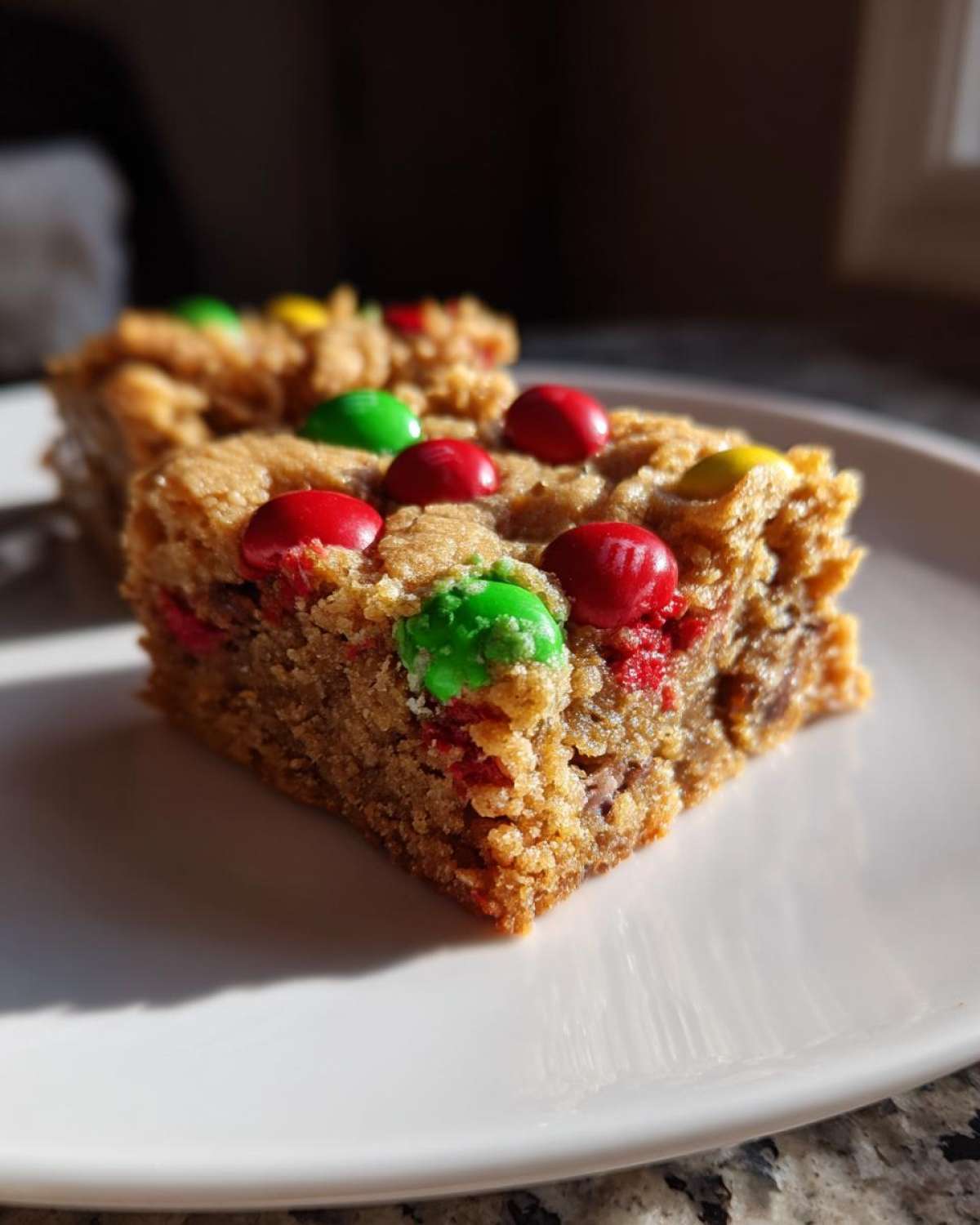 Close-up of two Christmas cookie bars topped with red, green, and yellow M&Ms on a white plate.