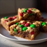 Close-up of delicious Christmas cookie bars topped with red and green M&Ms on a white plate.