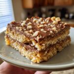 Close-up of two Christmas toffee squares stacked on a plate, topped with chocolate and chopped nuts.