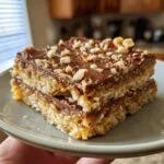 Close-up of two Christmas toffee squares stacked on a plate, topped with chocolate and chopped nuts.