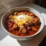A steaming bowl of savory chuck roast chili topped with shredded cheese and a dollop of sour cream.