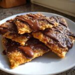 A stack of crispy churro cracker candy pieces drizzled with melted chocolate and sprinkled with sugar.
