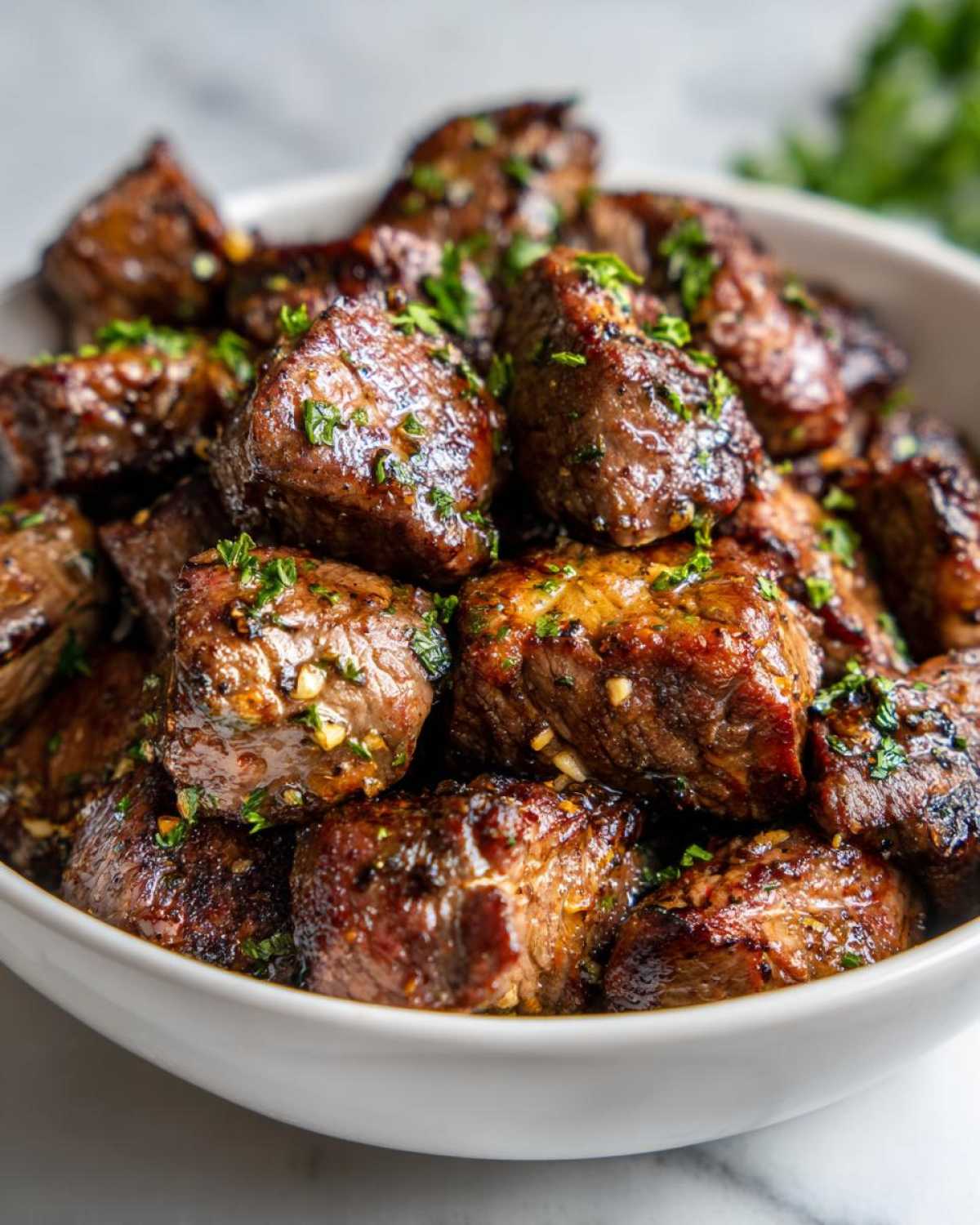 Close-up of a white bowl filled with juicy cowboy butter steak bites, garnished with fresh parsley.