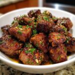 A close-up of a white bowl filled with juicy Cowboy Butter Steak Bites, glistening with sauce and topped with fresh parsley.