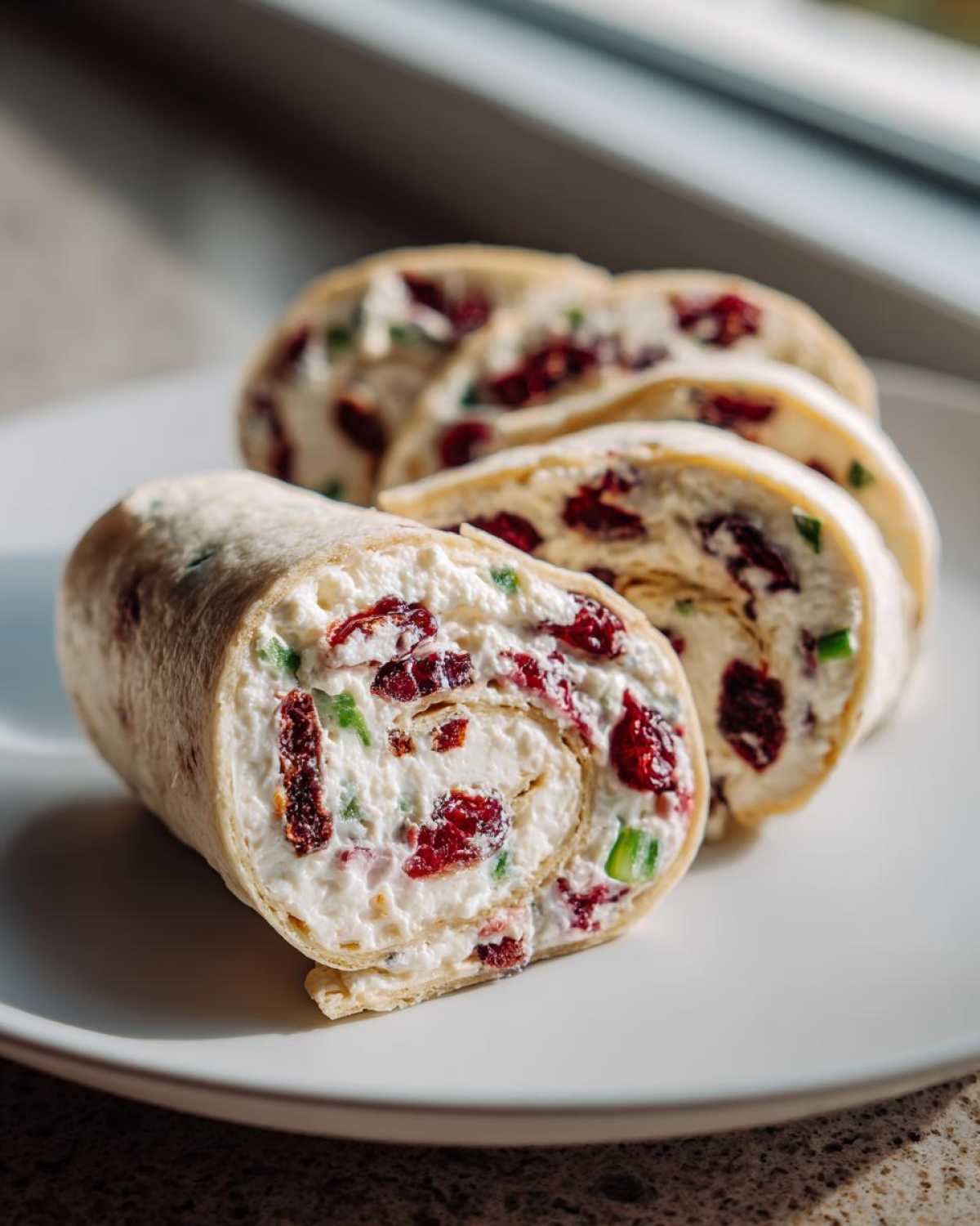 Close-up of delicious Cranberry roll ups filled with cream cheese and dried cranberries, sliced on a white plate.
