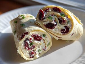 Close-up of two halves of a cranberry roll up, showing the creamy filling with dried cranberries and green onions.
