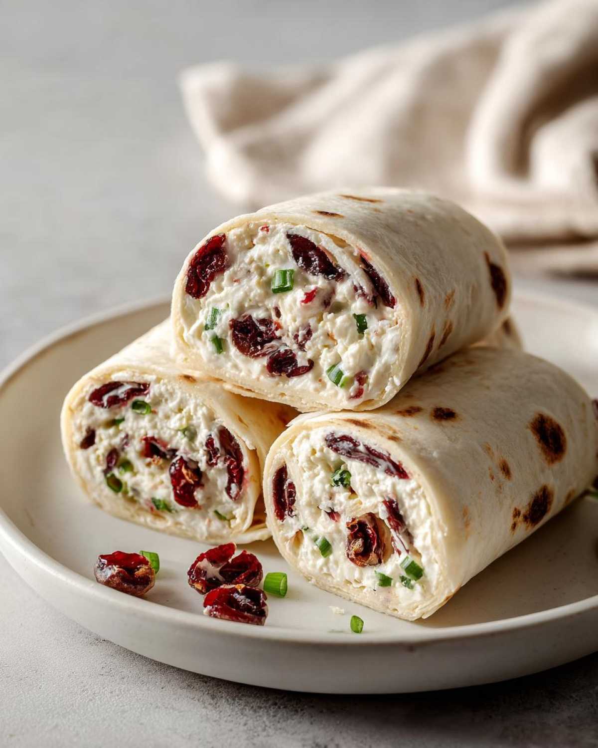 Close-up of three cranberry roll ups filled with cream cheese, dried cranberries, and chives on a white plate.