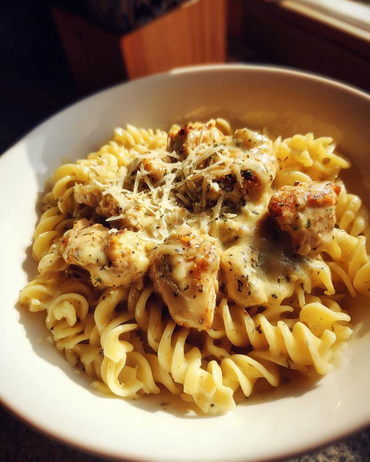 A bowl of creamy garlic parmesan chicken pasta with fusilli noodles and topped with shredded parmesan cheese.