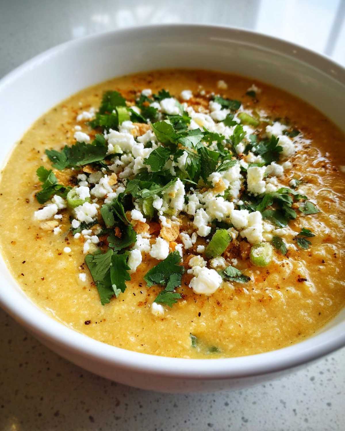 A close-up of a creamy bowl of mexican street corn soup garnished with cotija cheese, cilantro, and spices.