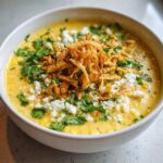 A close-up of creamy mexican street corn soup topped with cotija cheese, cilantro, and crispy fried onions.