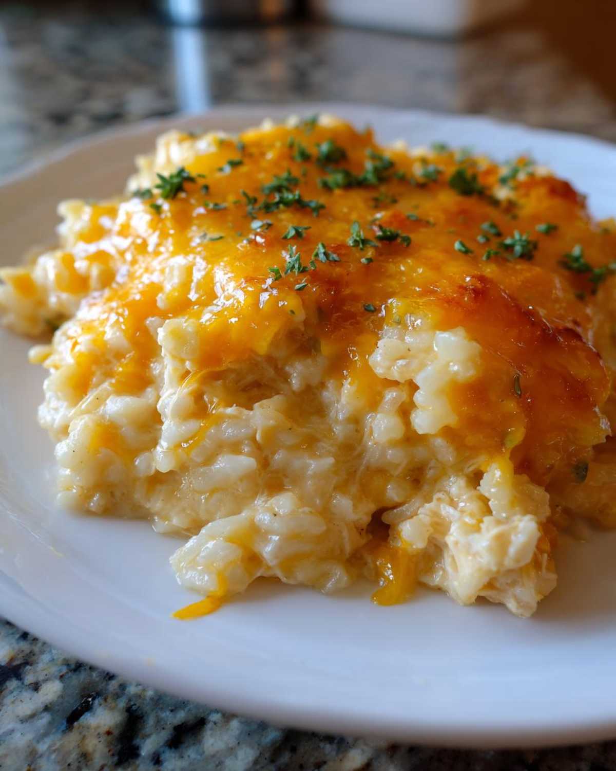 A close-up of a serving of creamy rice casserole topped with melted orange cheddar cheese and fresh parsley.
