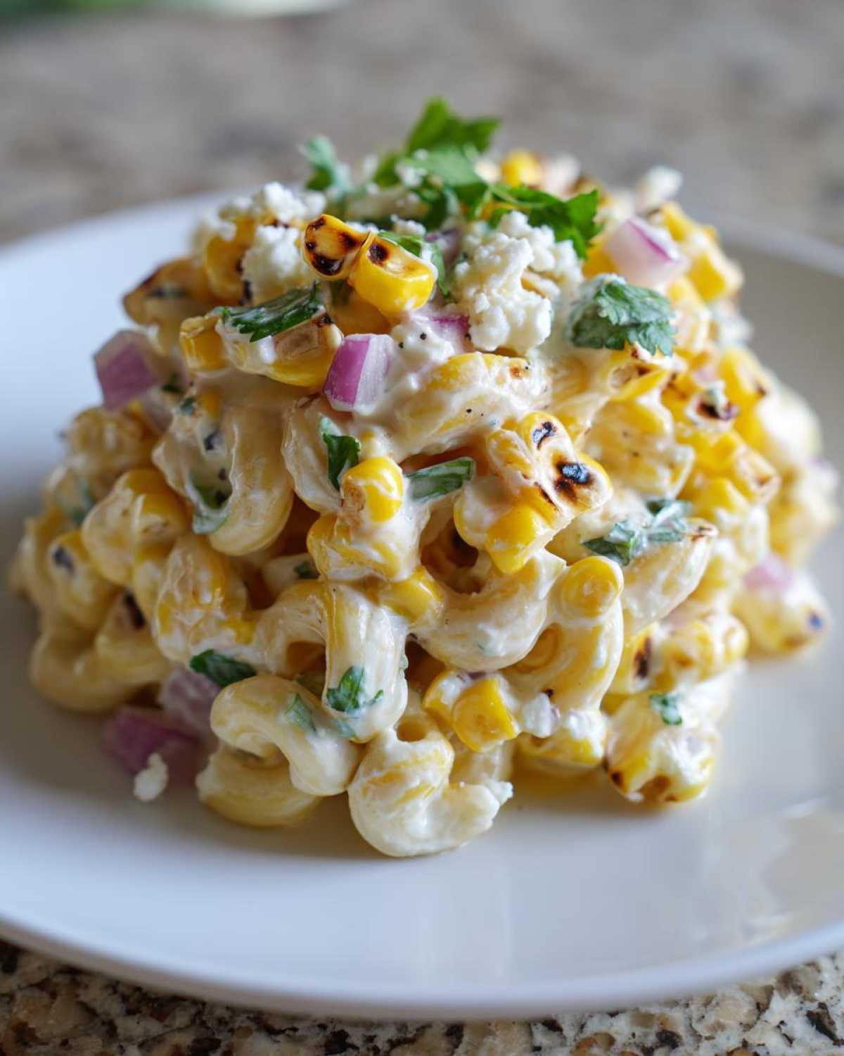A close-up of creamy street corn pasta salad featuring charred corn, red onion, and cotija cheese.