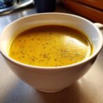 A close-up of a steaming bowl of creamy vegetable soup, garnished with herbs.