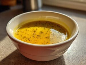 A close-up of a bowl of vibrant yellow creamy vegetable soup, seasoned with herbs.
