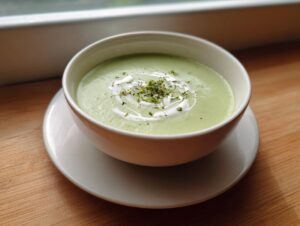 A bowl of vibrant green zucchini soup, garnished with a swirl of cream and dried herbs.