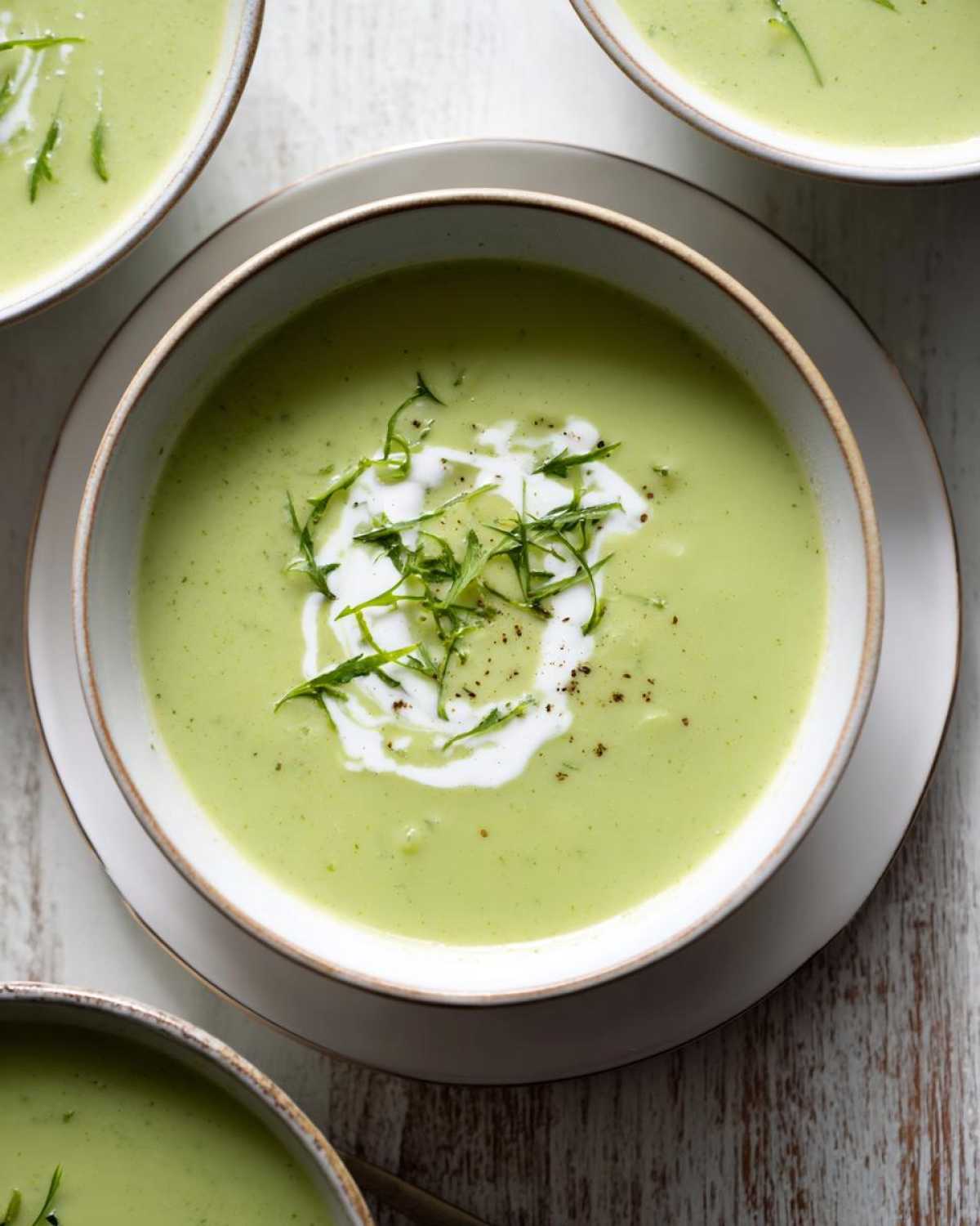 Overhead view of a creamy green zucchini soup garnished with cream swirl and fresh herbs.