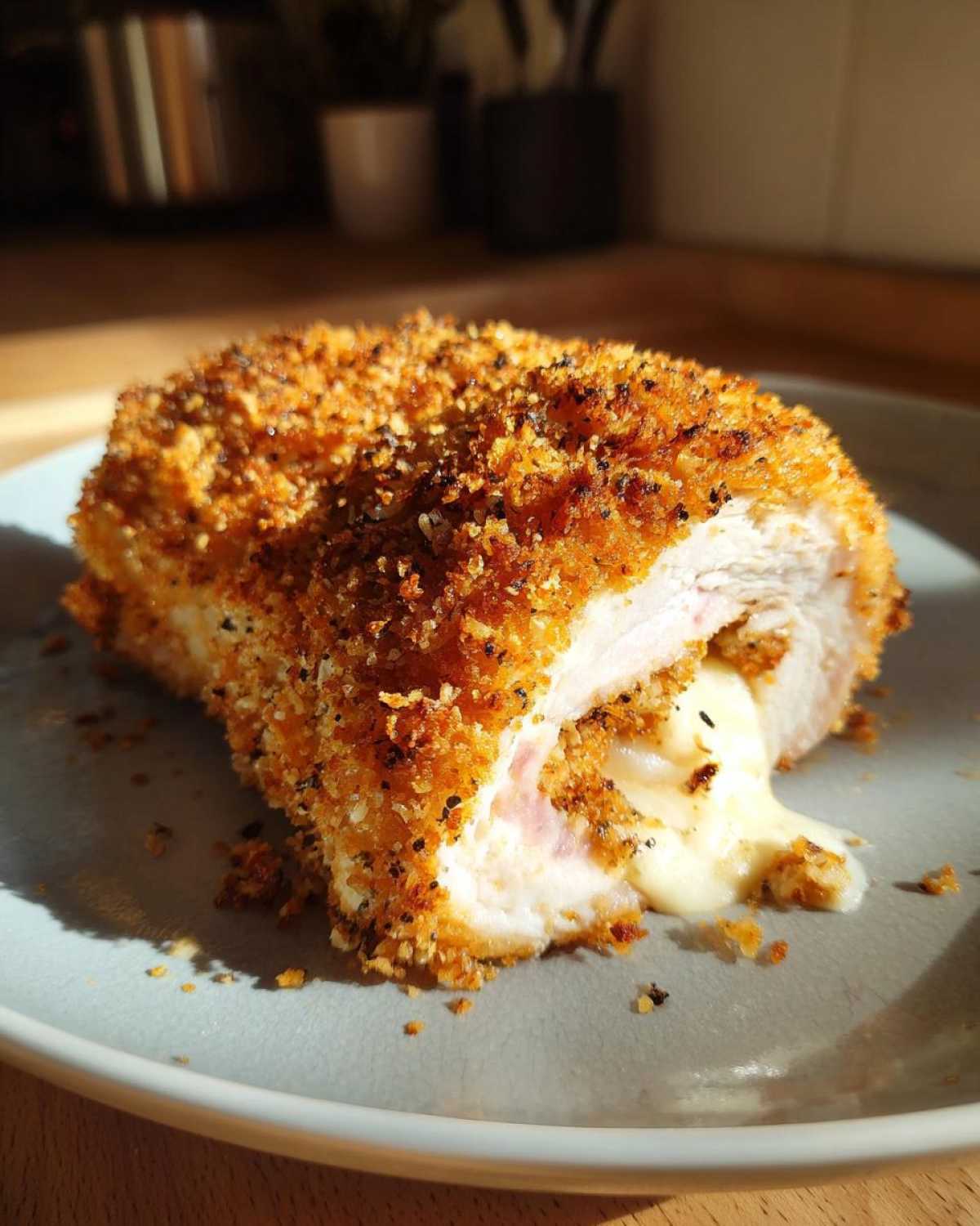 A close-up of a crispy Chicken Cordon Bleu on a plate, with melted cheese oozing out.