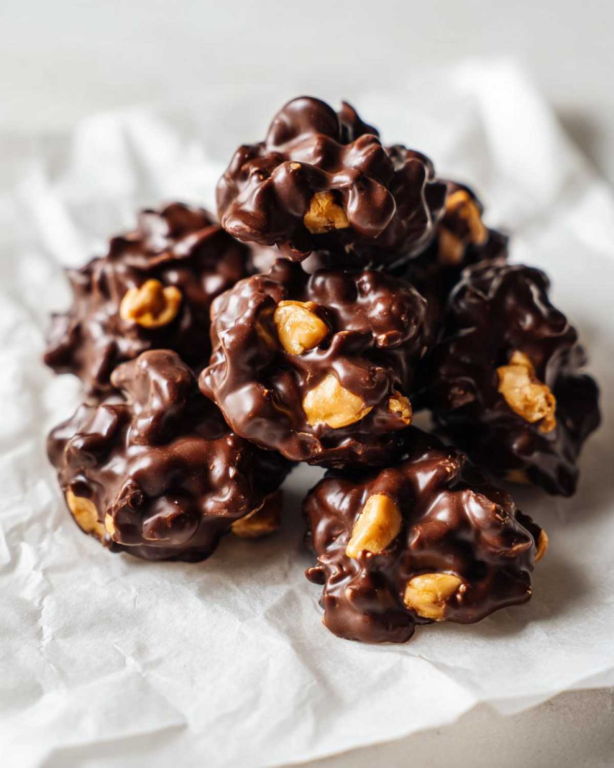 A close-up, overhead view of a pile of rich, dark chocolate crockpot candy clusters with visible peanuts.