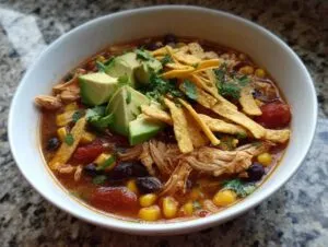 A bowl of hearty crockpot chicken tortilla soup topped with fresh avocado, crispy tortilla strips, and cilantro.