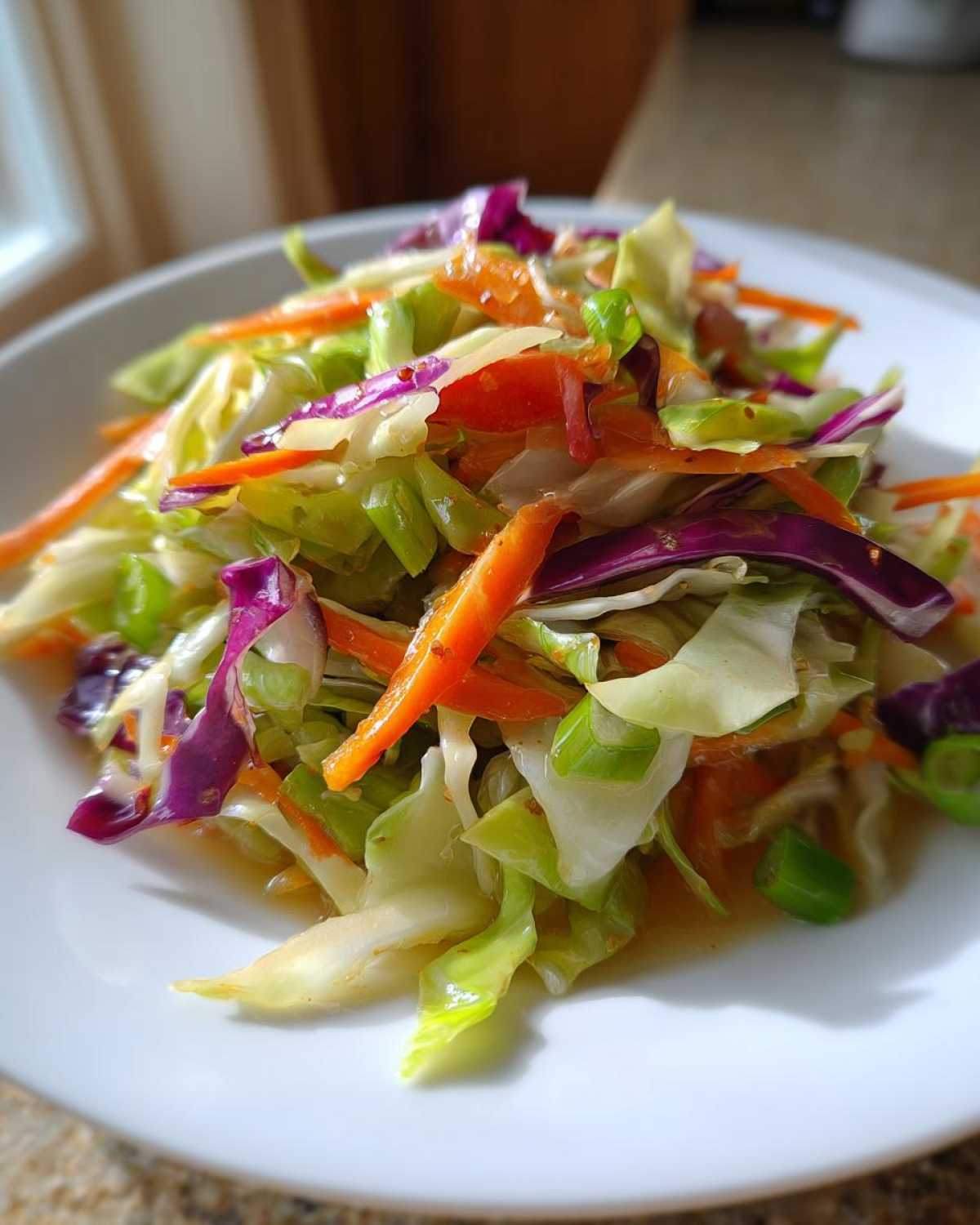 Close-up of a vibrant cabbage salad featuring shredded green and purple cabbage and bright orange carrots.