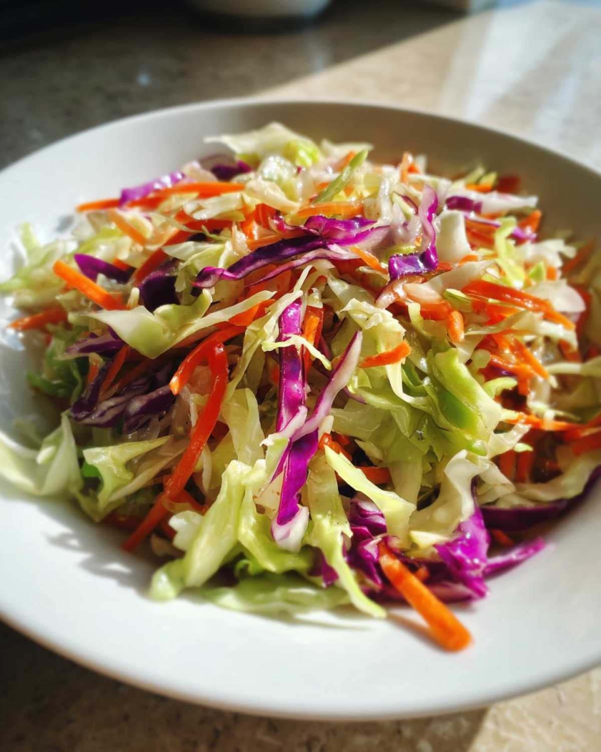 Close-up of a vibrant cabbage salad featuring shredded green cabbage, red cabbage, and carrots, highlighting its crunchiness.
