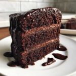 A thick slice of rich, three-layer death by chocolate cake, generously topped with chocolate ganache.