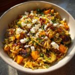 A bowl of delicious fall orzo salad topped with roasted butternut squash, Brussels sprouts, feta cheese, and herbs.