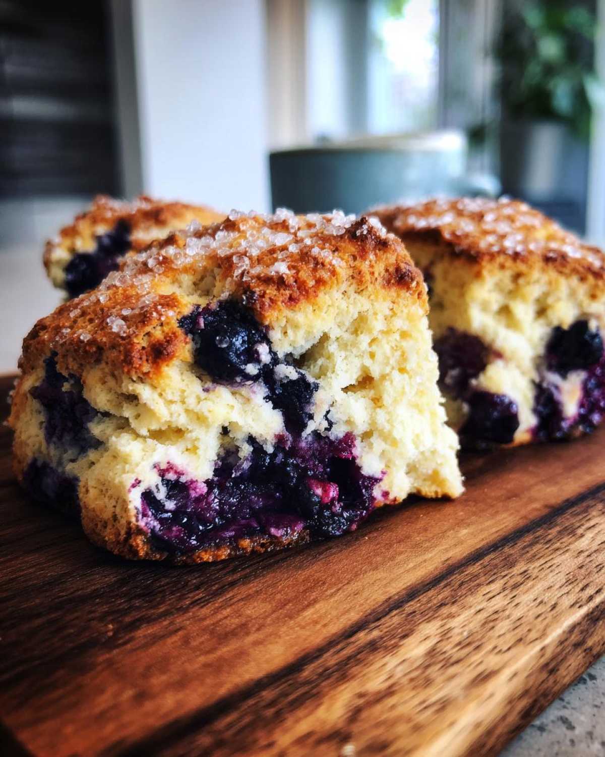 Close-up of fluffy blueberry scones with a sparkling sugar topping on a wooden board.