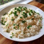 A white bowl filled with fluffy rice pilaf recipe, garnished generously with fresh chopped parsley.