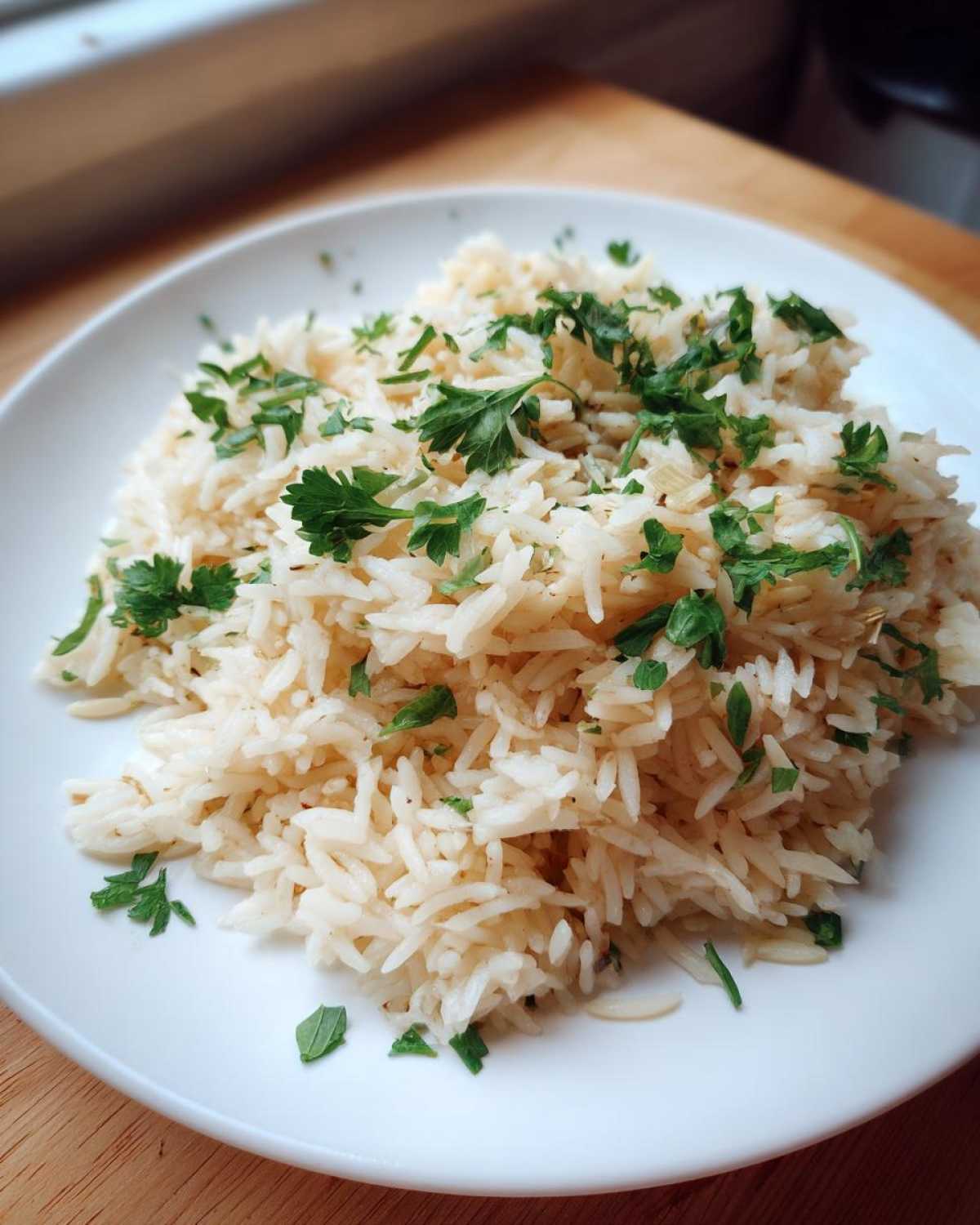 A serving of fluffy, perfectly cooked rice pilaf recipe garnished generously with fresh chopped parsley on a white plate.