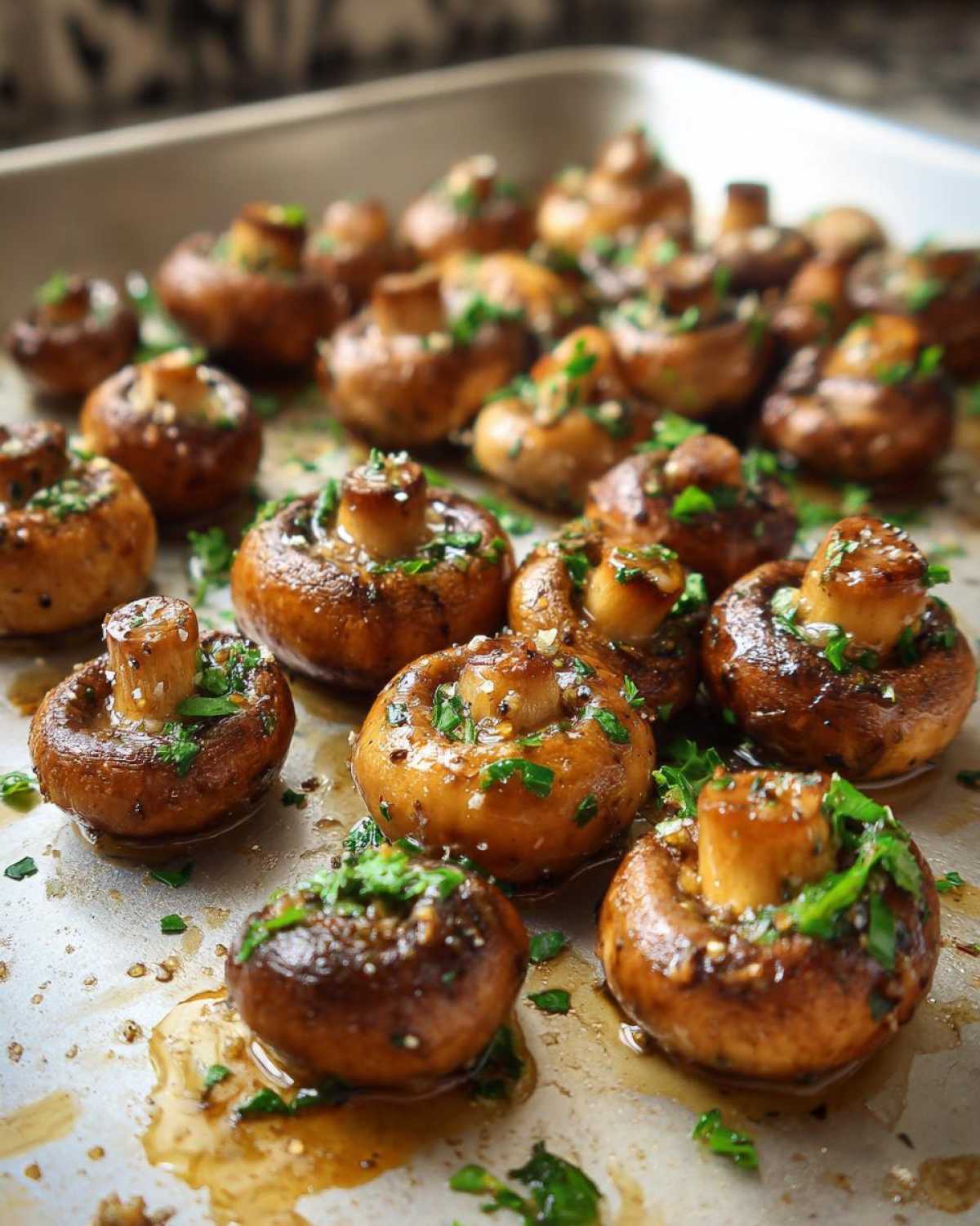 Close-up of glistening garlic butter mushrooms, baked on a sheet pan and sprinkled with fresh parsley.