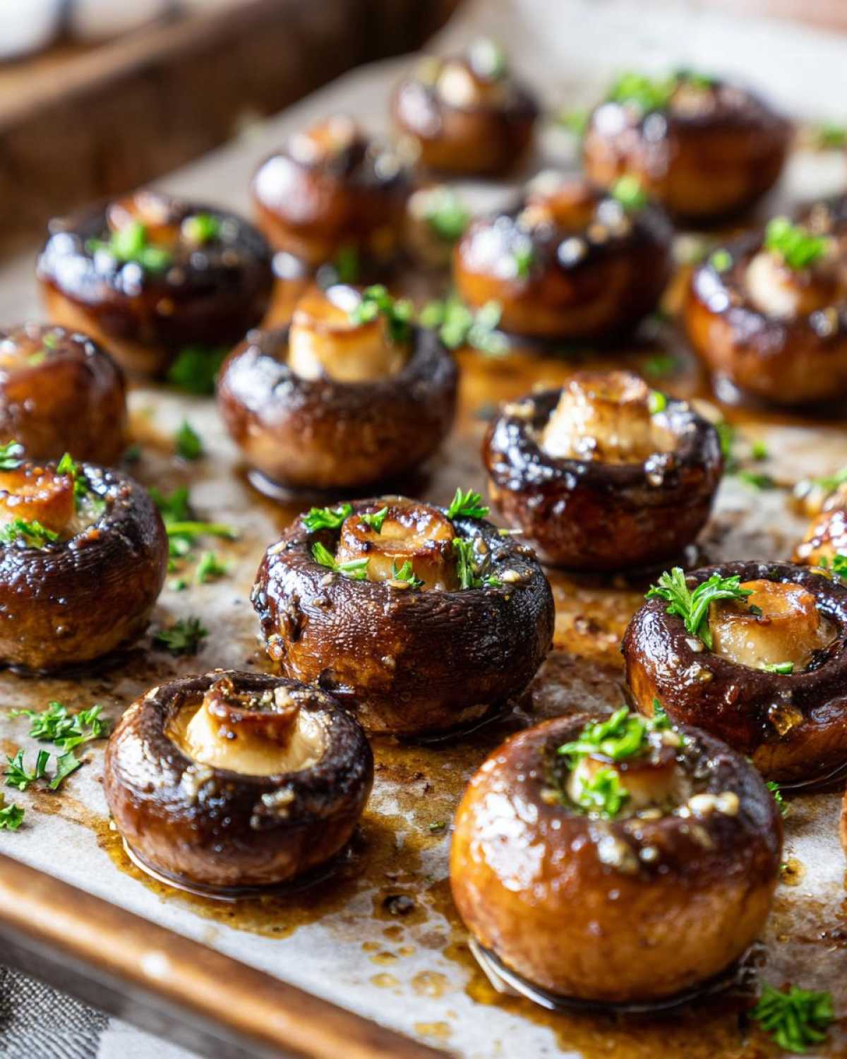 Close-up of glossy garlic butter mushrooms, glistening with sauce and topped with fresh parsley, arranged on a baking sheet.