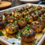 Close-up of roasted garlic butter mushrooms, glistening with butter and topped with fresh parsley, on a baking sheet.