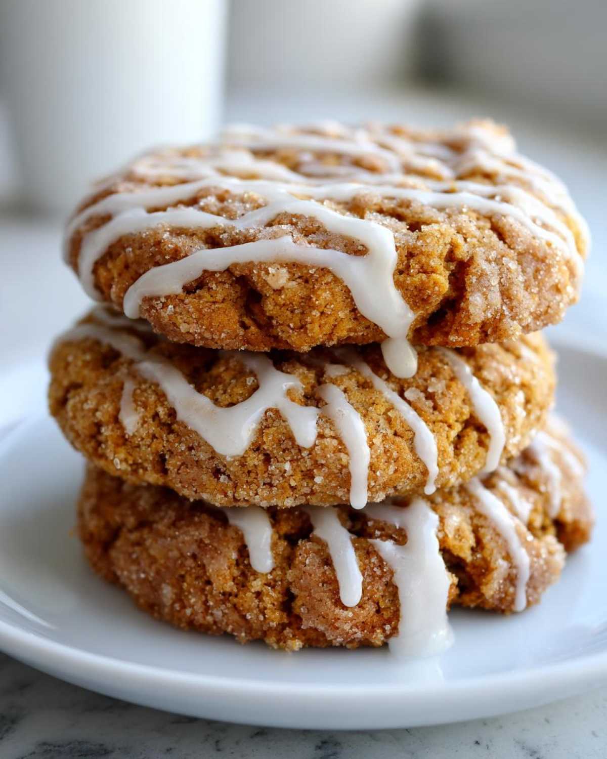 A stack of three soft, cinnamon-sugar coated coffee cake cookies drizzled with white vanilla glaze.