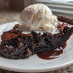 A decadent slice of hot fudge pie topped with a scoop of melting vanilla ice cream.