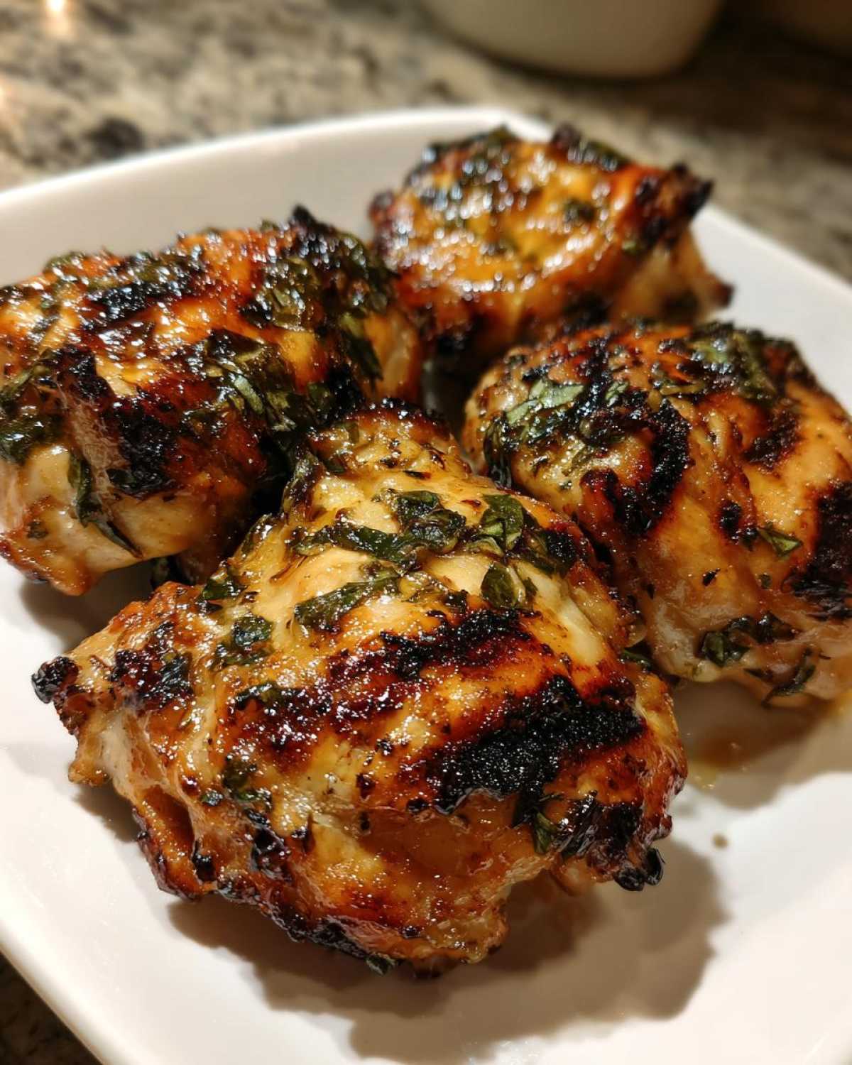 Close-up of four pieces of grilled coconut basil chicken on a white plate, showing grill marks and herbs.