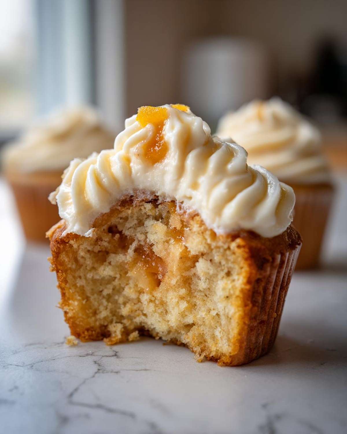 Close-up of a Honey Peach Cream Cheese Cupcake with a bite taken out, showing the moist interior and creamy frosting.