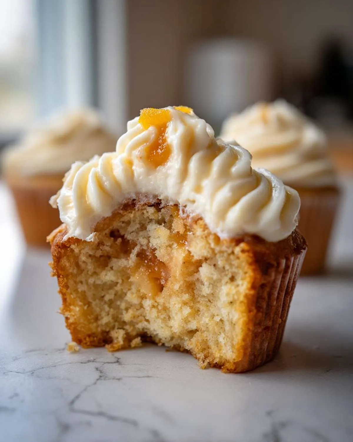 Close-up of a Honey Peach Cream Cheese Cupcake with a bite taken out, showing the moist interior and creamy frosting.