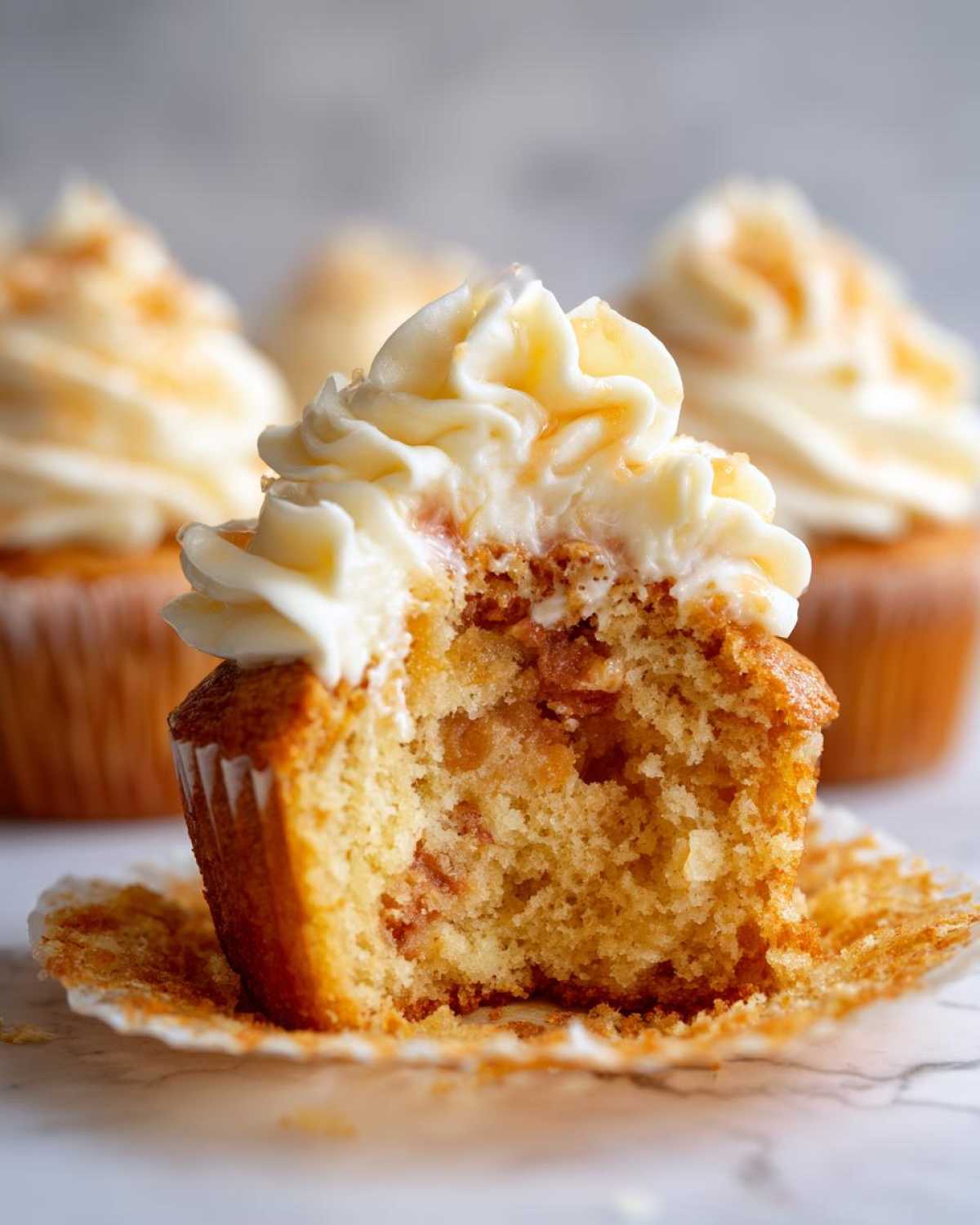 A bite taken out of a Honey Peach Cream Cheese Cupcake, showing the moist crumb and peach filling.