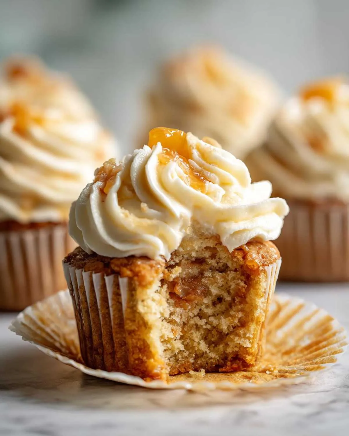 Close-up of a Honey Peach Cream Cheese Cupcake with a bite taken out, showing the moist interior and creamy frosting.