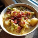 A close-up bowl of Irish bacon cabbage potato soup, topped with crispy bacon bits and black pepper.
