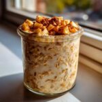 A glass jar filled with creamy apple cinnamon overnight oats, topped with diced apples and a sprinkle of cinnamon.