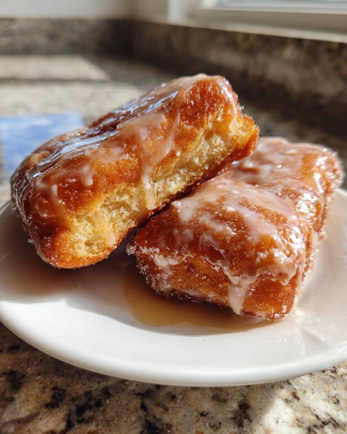 Close-up of two irresistible maple donut bars, one cut in half, showing a fluffy interior and drizzled with a sweet maple glaze.