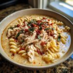 A close-up of a bowl of creamy Marry Me Chicken Soup, featuring shredded chicken, rotini pasta, and a garnish of herbs and sun-dried tomatoes.
