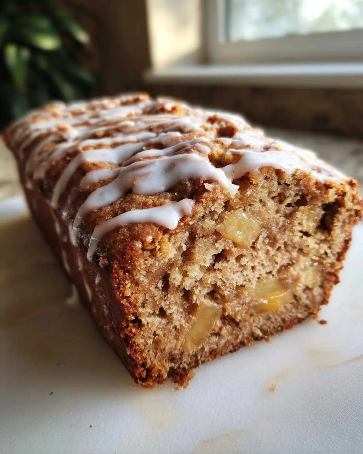 Close-up of a moist apple cake loaf, showing chunks of baked apple inside and drizzled with white vanilla icing.