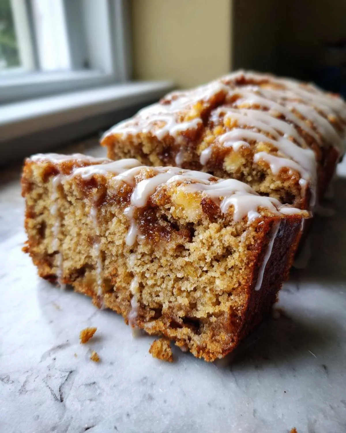 Close-up of a moist apple cake loaf, sliced, showing texture and drizzled with white icing.