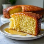 Close-up of a moist slice of olive oil cake drizzled with a shiny glaze, sitting on a white plate.