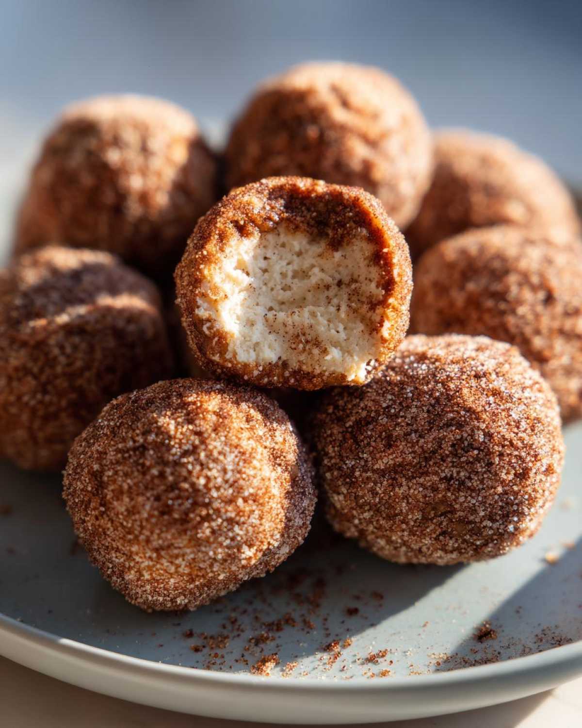 A close-up of no bake pumpkin cheesecake balls coated in cinnamon sugar, with one ball bitten into.